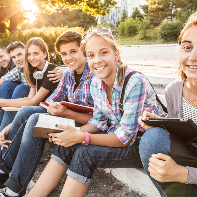 Group,Of,Young,Students,With,Books,And,Gadgets,Sit,On